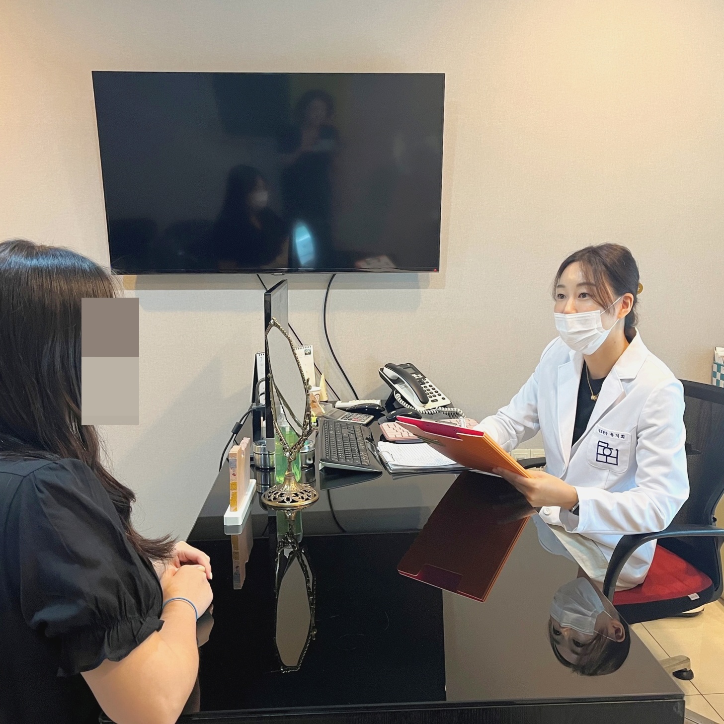 마주 앉은 환자에게 차트를 들고 설명하는 상담 장면